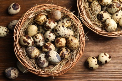 Photo of Wicker bowls, quail eggs and straw on wooden table, flat lay