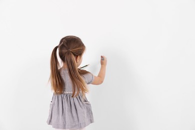 Photo of Little girl drawing on white wall indoors, back view. Space for text