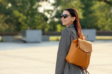 Beautiful young woman with stylish backpack on city street, space for text