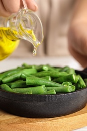 Photo of Woman pouring oil onto green beans at table, closeup