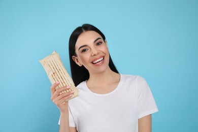 Happy young woman with delicious shawarma on light blue background