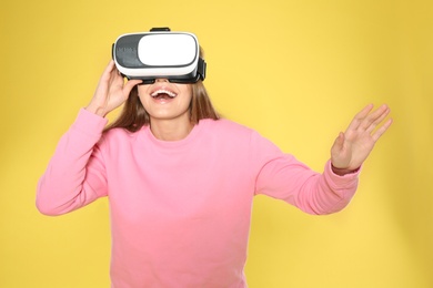 Emotional young woman playing video games with virtual reality headset on color background