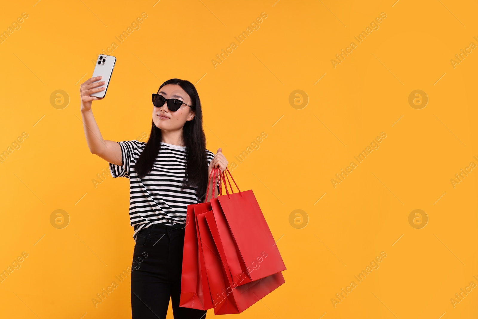 Photo of Beautiful woman with shopping bags taking selfie on yellow background. Space for text