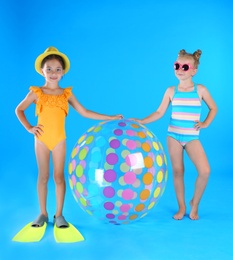 Cute little children in beachwear with inflatable ball on light blue background