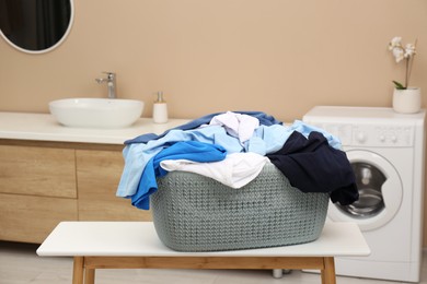 Photo of Plastic laundry basket overfilled with clothes on white table in bathroom
