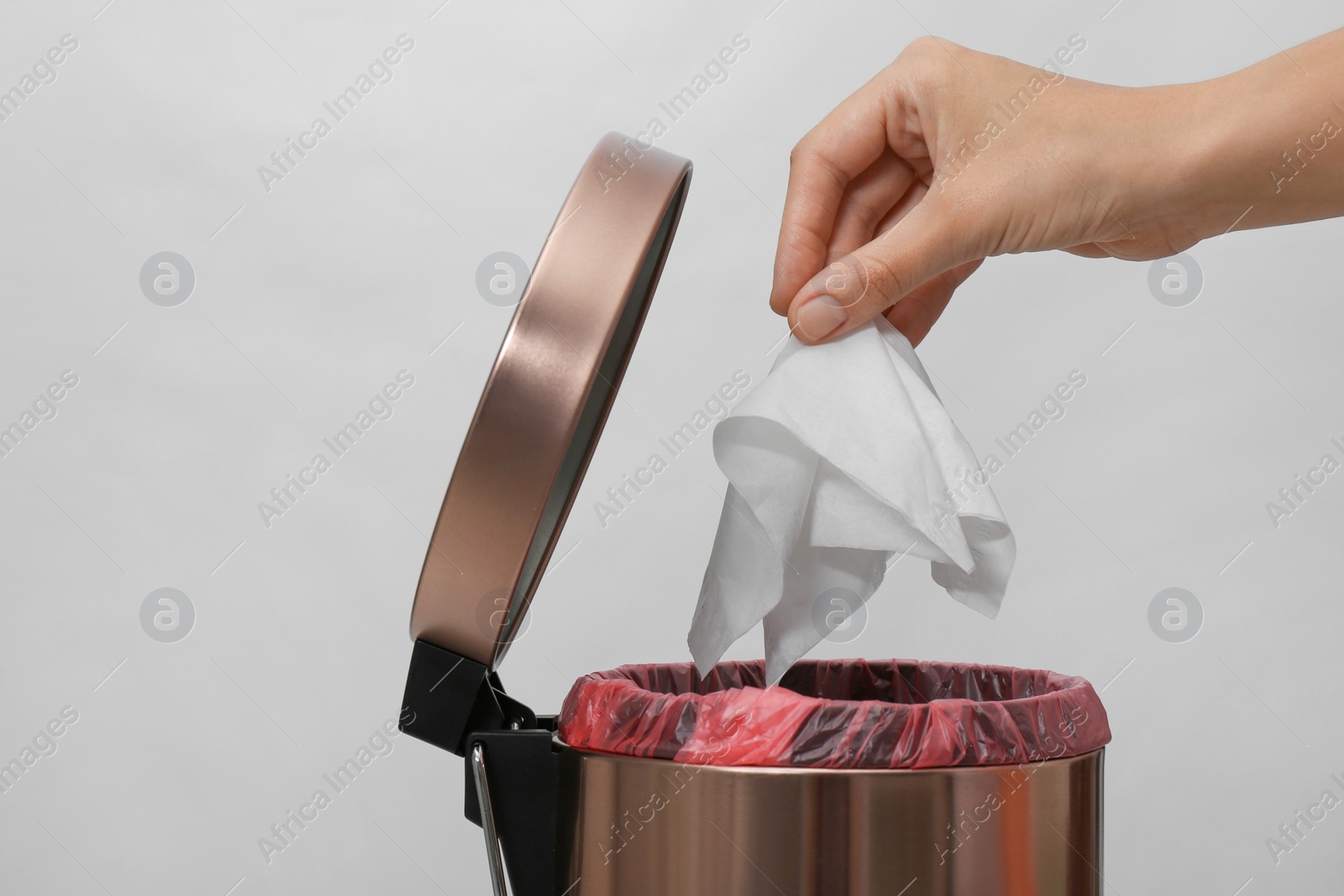 Photo of Woman putting paper tissue into trash bin on light background, closeup