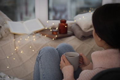 Photo of Woman with hot drink relaxing near window at home. Cozy season