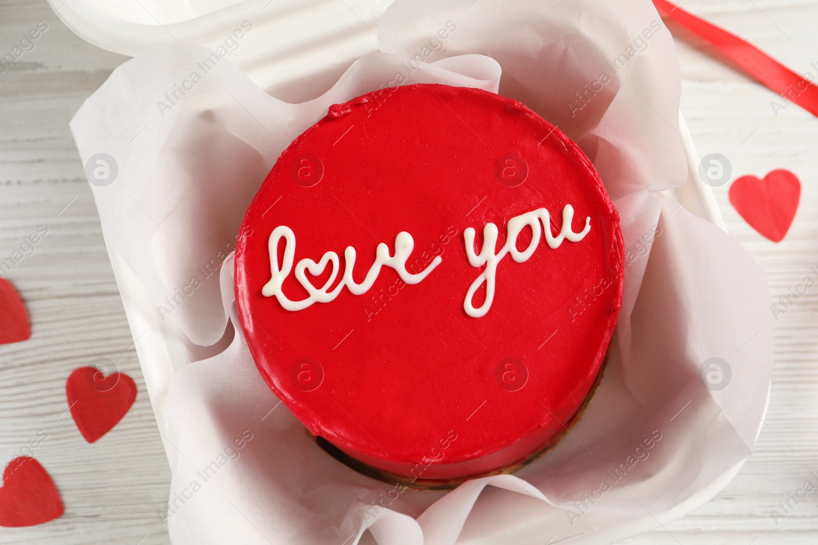 Photo of Bento cake with Love You text in takeaway box and paper hearts on white wooden table, flat lay. St. Valentine's day surprise