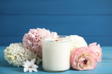 Scented candle with burning wooden wick and flowers on blue table