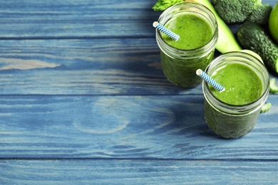 Photo of Delicious green juice and fresh ingredients on blue wooden table, space for text