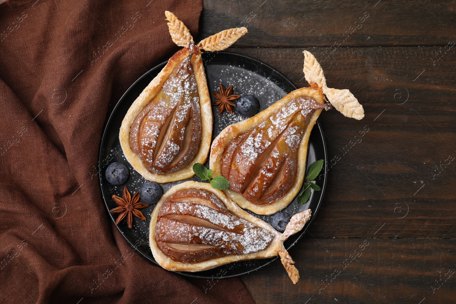 Photo of Delicious pears baked in puff pastry with powdered sugar served on wooden table, top view