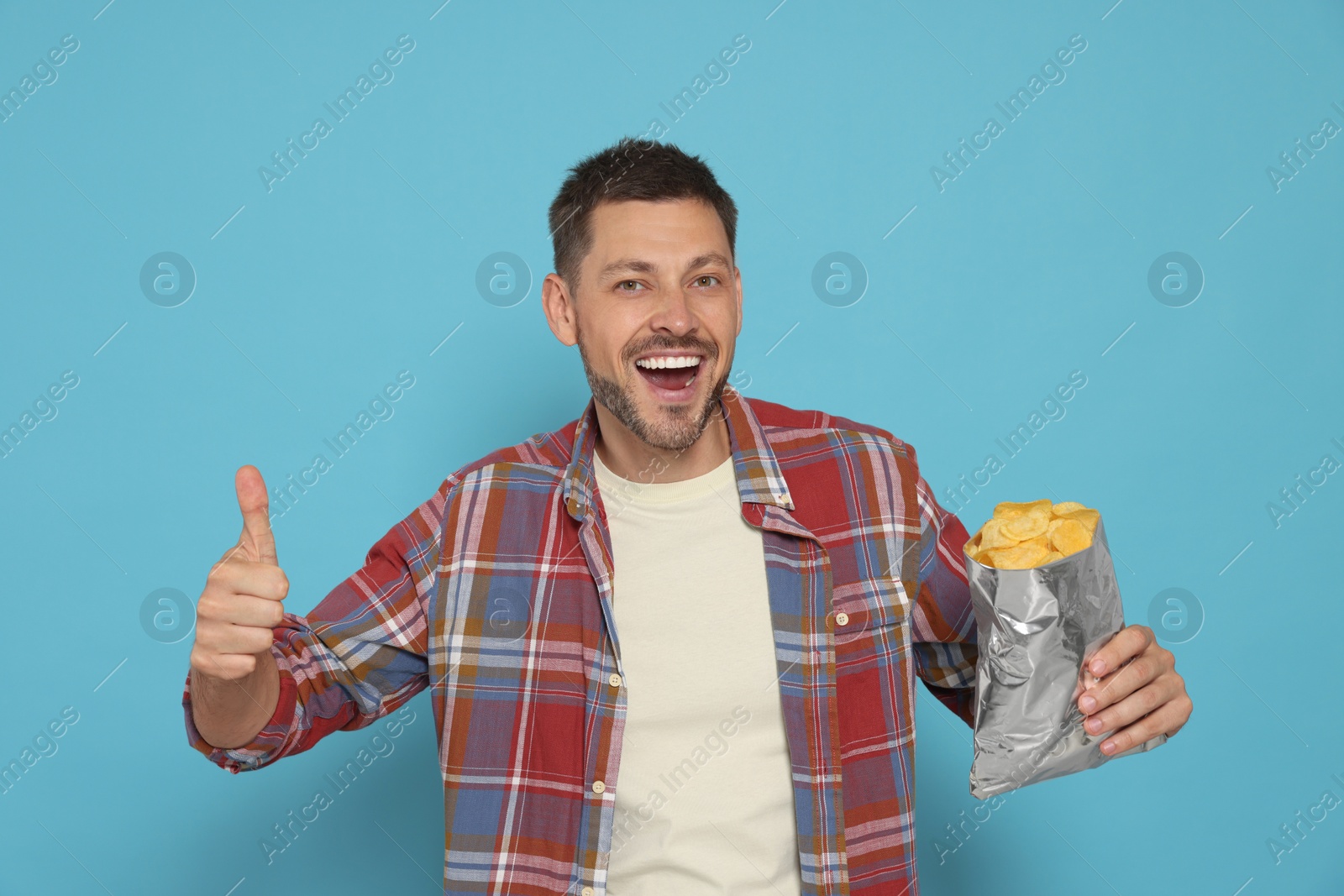 Photo of Handsome man with potato chips showing thumb up on light blue background