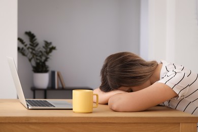 Photo of Woman sleeping in front of laptop at wooden table indoors