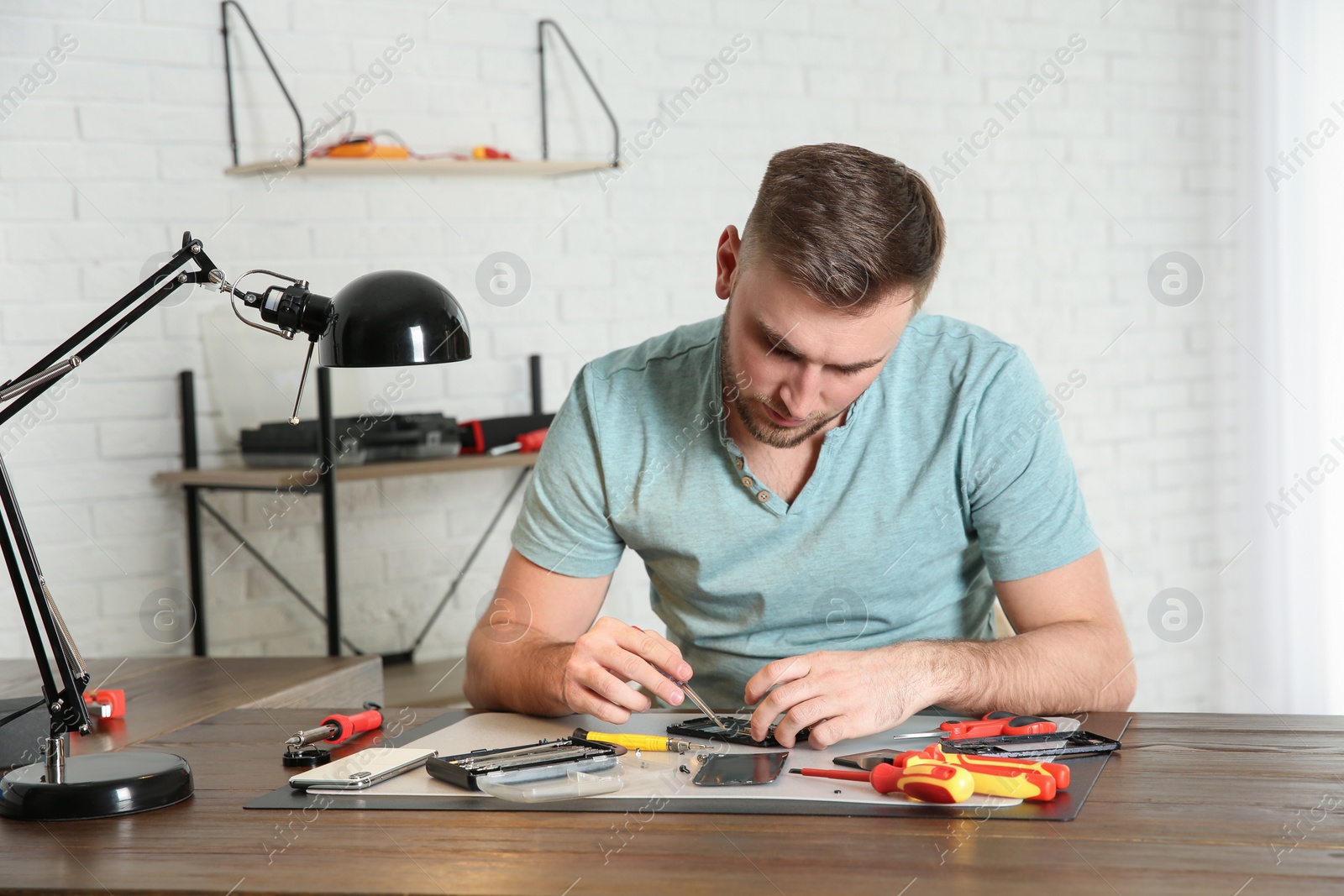 Photo of Technician repairing mobile phone at table in workshop