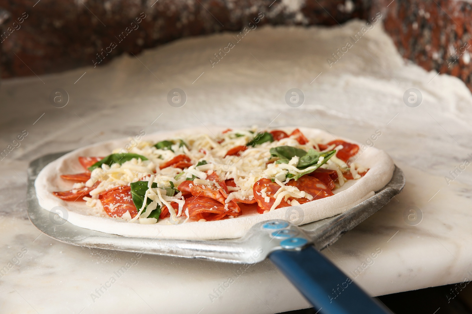 Photo of Peel with raw traditional Italian pizza on table in restaurant kitchen