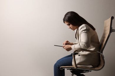 Photo of Young woman with bad posture using tablet while sitting on chair against grey background. Space for text