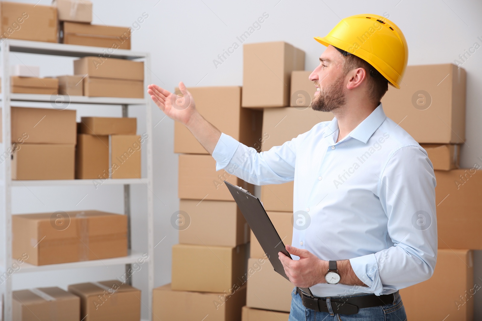 Photo of Young man with clipboard near cardboard boxes at warehouse