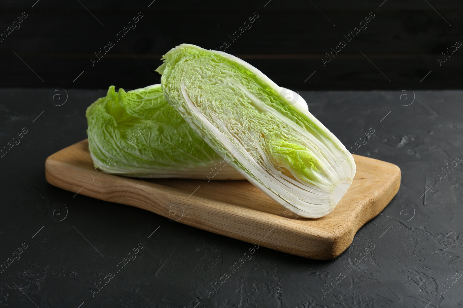 Photo of Whole and cut fresh Chinese cabbages on black textured table