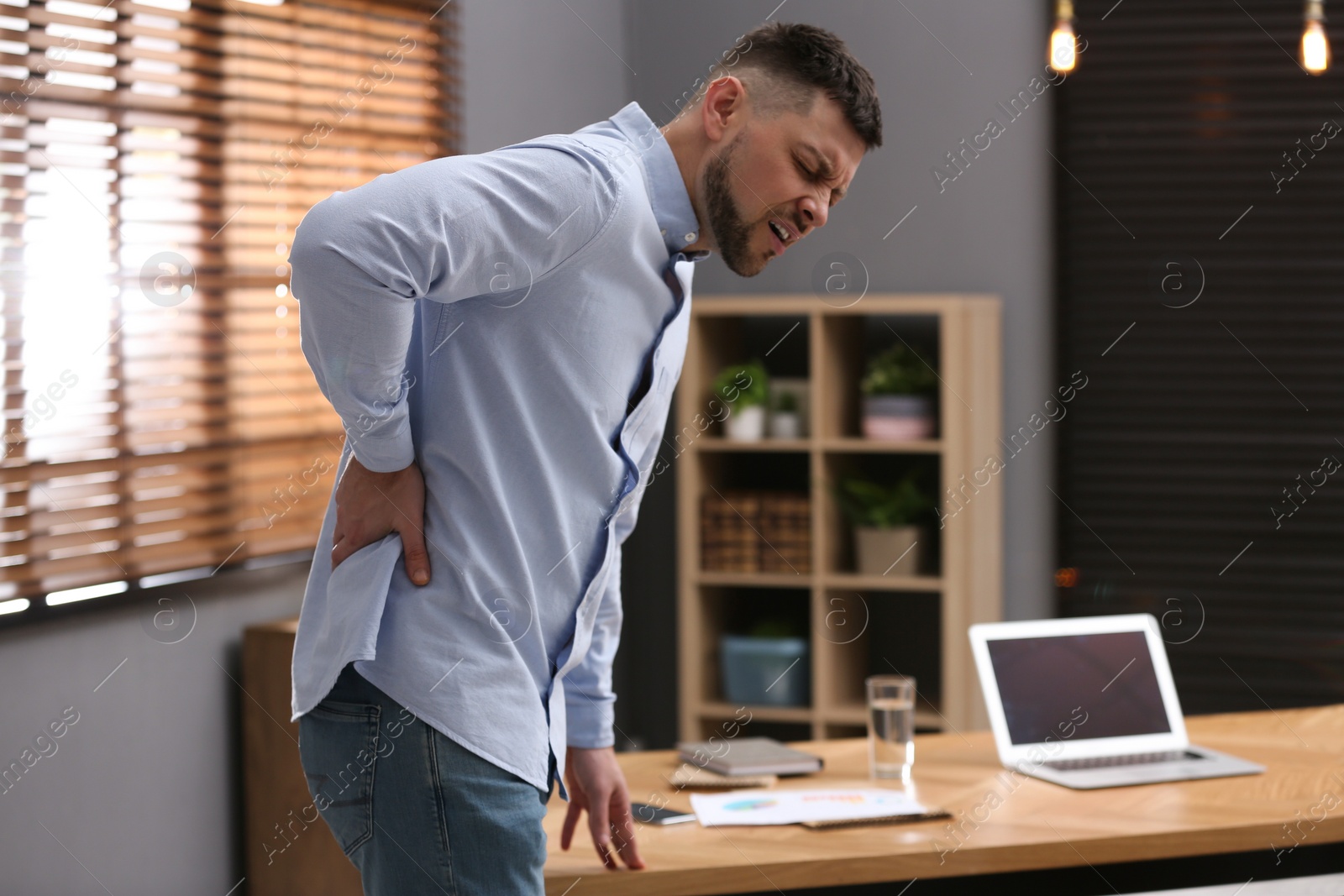 Photo of Man suffering from back pain in office. Symptom of poor posture