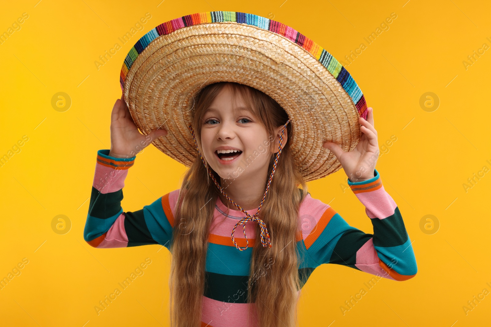Photo of Cute girl in Mexican sombrero hat on orange background