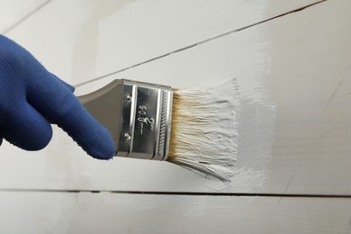Worker applying white paint onto wooden surface, closeup