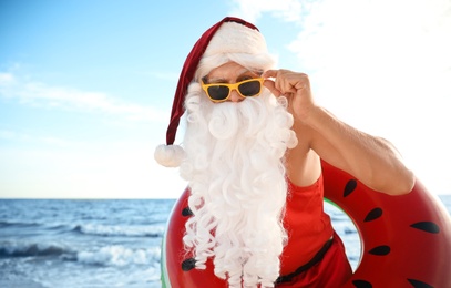 Photo of Santa Claus with inflatable ring on beach, space for text. Christmas vacation