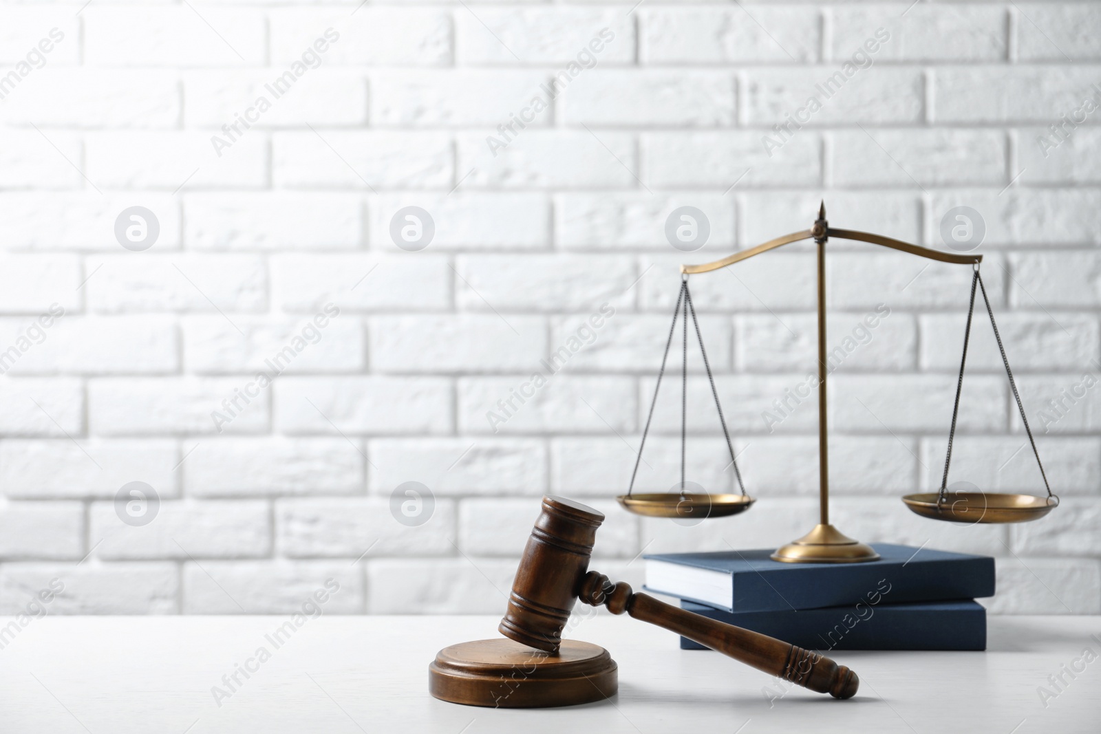 Photo of Scales of justice, wooden gavel and books on table against brick wall. Law concept