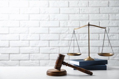 Scales of justice, wooden gavel and books on table against brick wall. Law concept