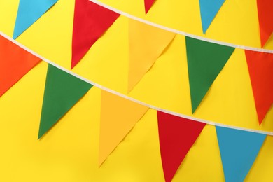 Photo of Bunting with colorful triangular flags on yellow background. Festive decor