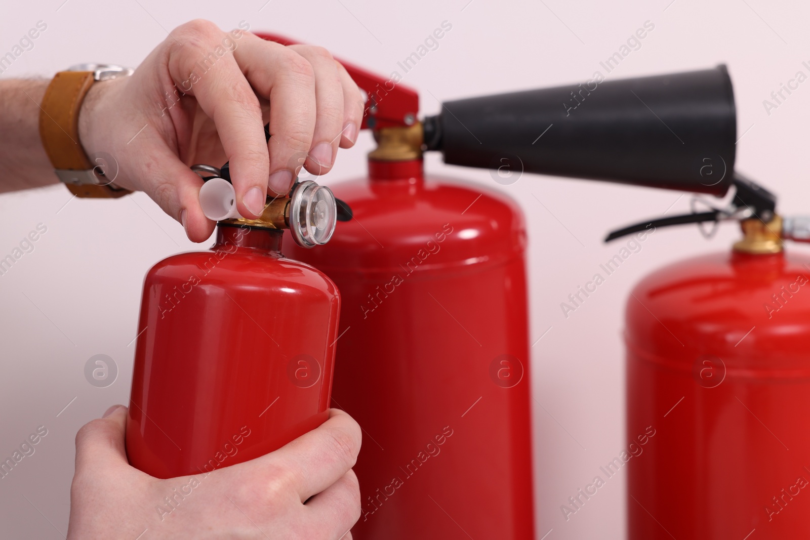 Photo of Man checking quality of fire extinguishers indoors, closeup