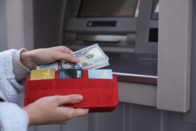 Photo of Woman putting money into wallet near cash machine outdoors, closeup