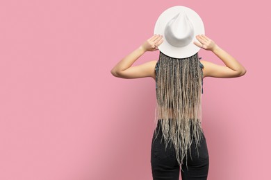 Photo of Woman with long african braids and hat on pink background, back view. Space for text