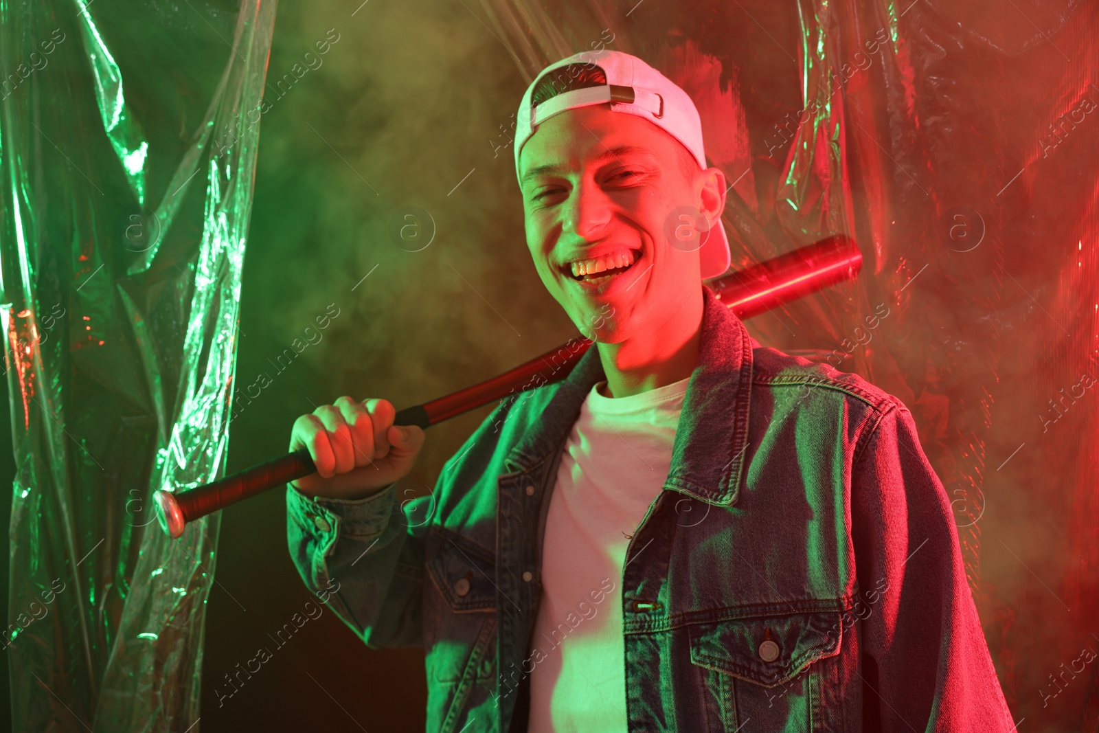 Photo of Young man with baseball bat on color background in neon lights