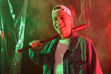 Young man with baseball bat on color background in neon lights