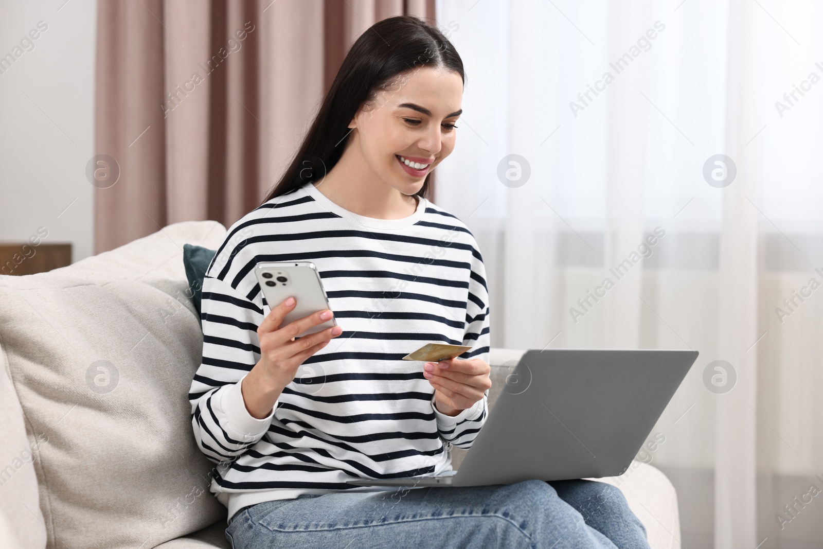 Photo of Happy young woman with credit card and gadgets shopping online at home