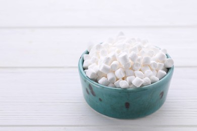 Photo of Bowl with delicious marshmallows on white wooden table