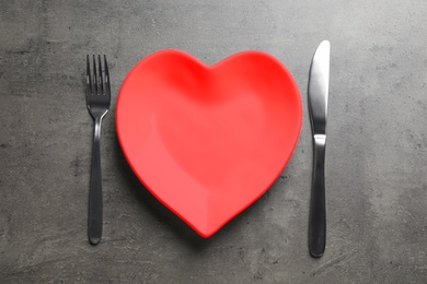 Photo of Heart shaped plate, fork and knife on grey background, flat lay