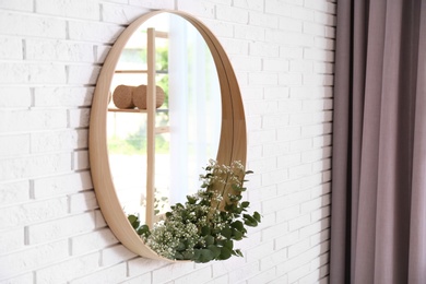 Photo of Round mirror with green branches on brick wall in modern room interior