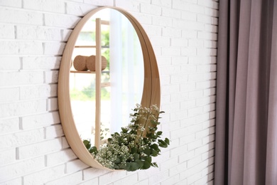 Round mirror with green branches on brick wall in modern room interior