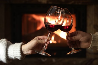 Couple clinking glasses of wine near fireplace at home, closeup