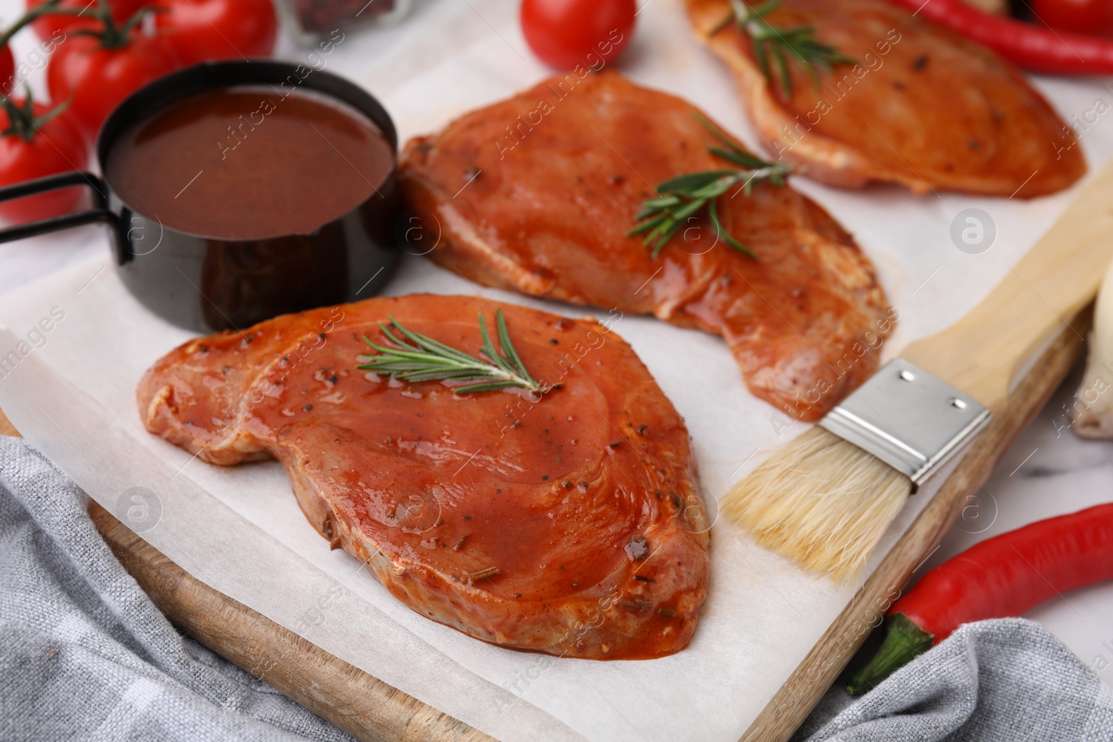 Photo of Raw marinated meat, rosemary and basting brush on table, closeup