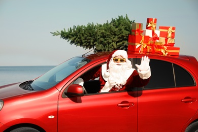 Authentic Santa Claus with presents and fir tree on roof driving modern car near sea