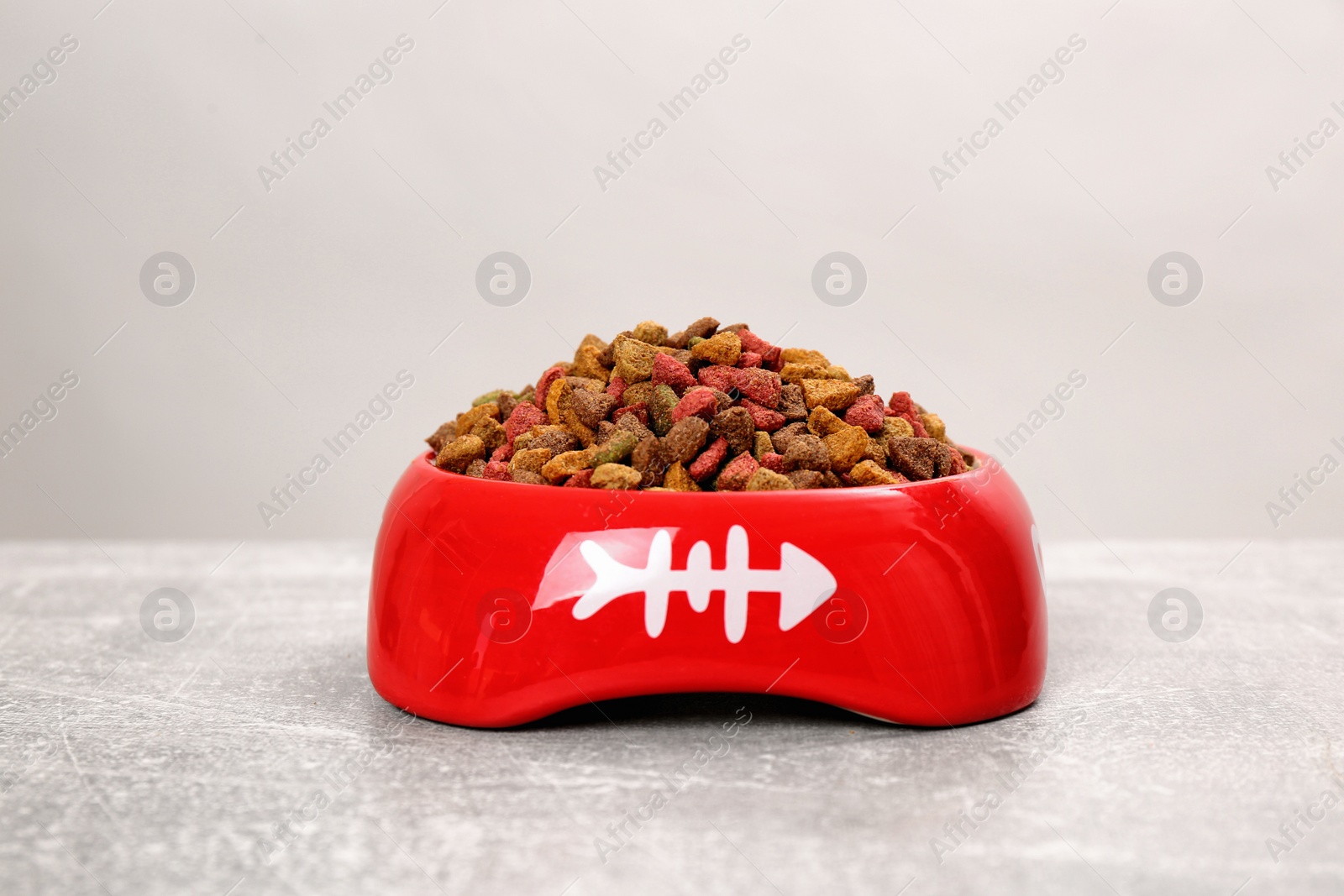 Photo of Dry cat food in red pet bowl on grey surface