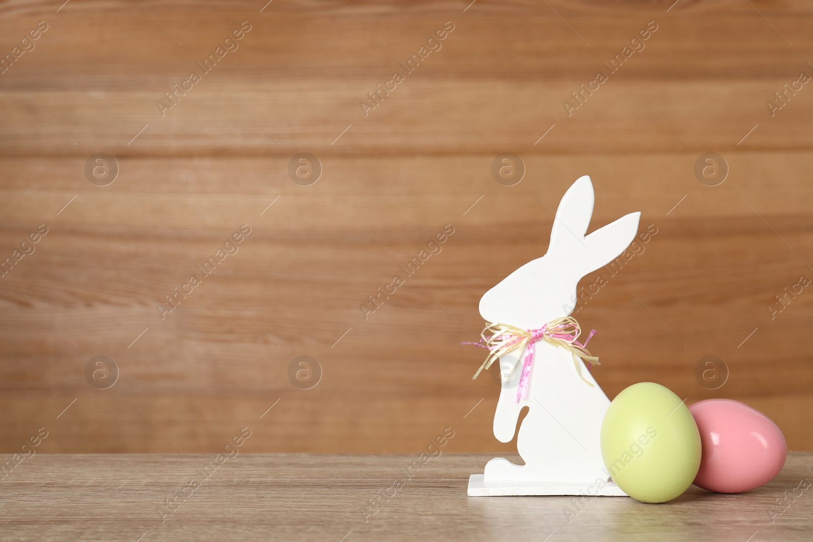 Photo of Cute Easter bunny figure and dyed eggs on table against wooden background, space for text