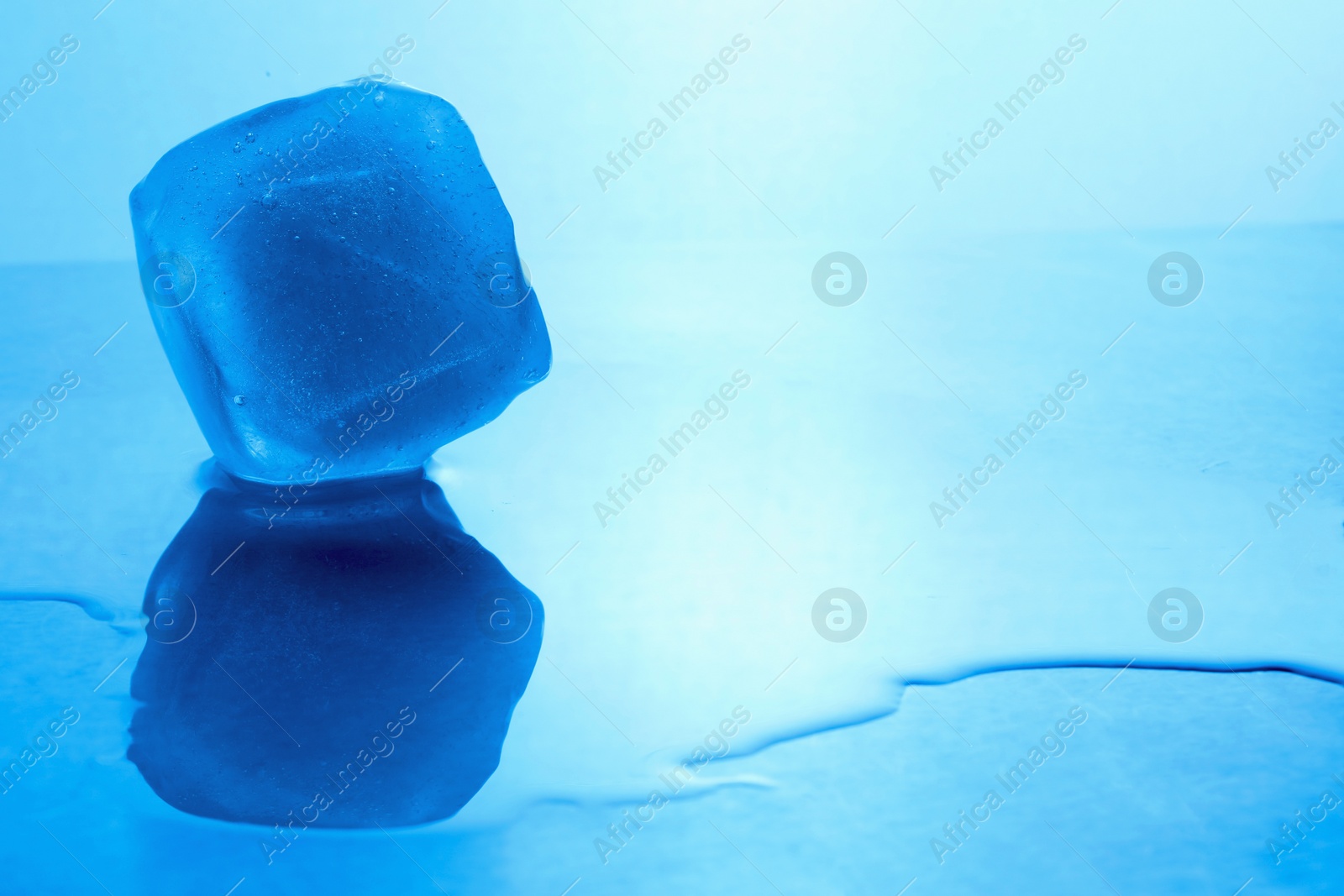 Photo of Crystal clear ice cube on light blue background, space for text. Color tone effect