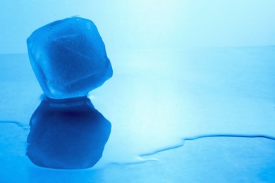 Photo of Crystal clear ice cube on light blue background, space for text. Color tone effect