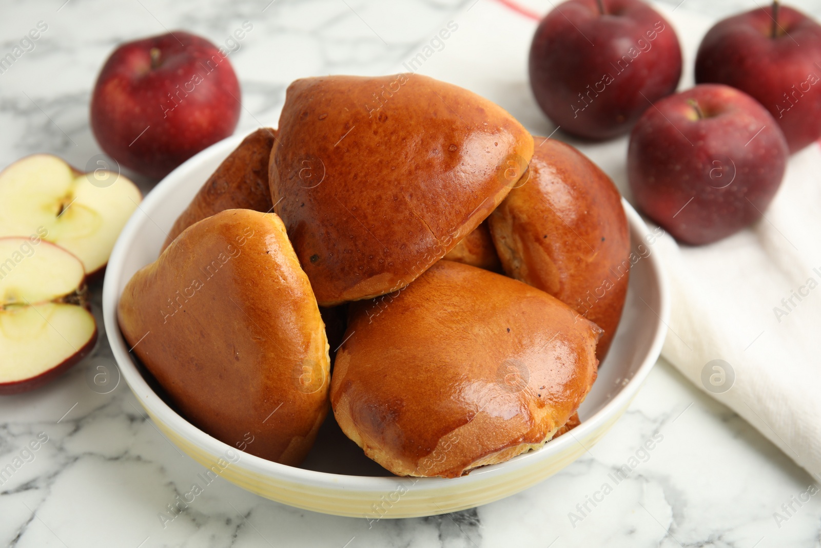 Photo of Delicious baked apple pirozhki in bowl and fruits on white marble table