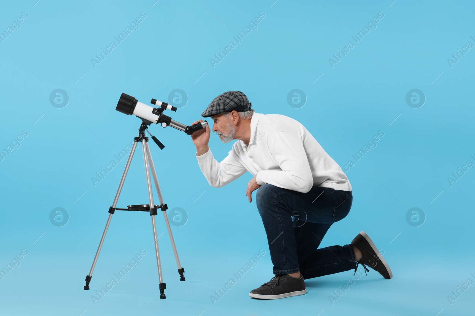 Photo of Senior astronomer looking at stars through telescope on light blue background