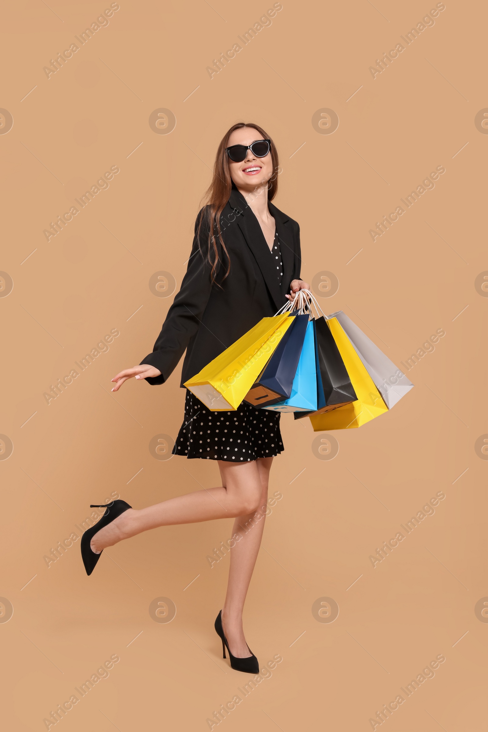 Photo of Stylish young woman in sunglasses with shopping bags on beige background