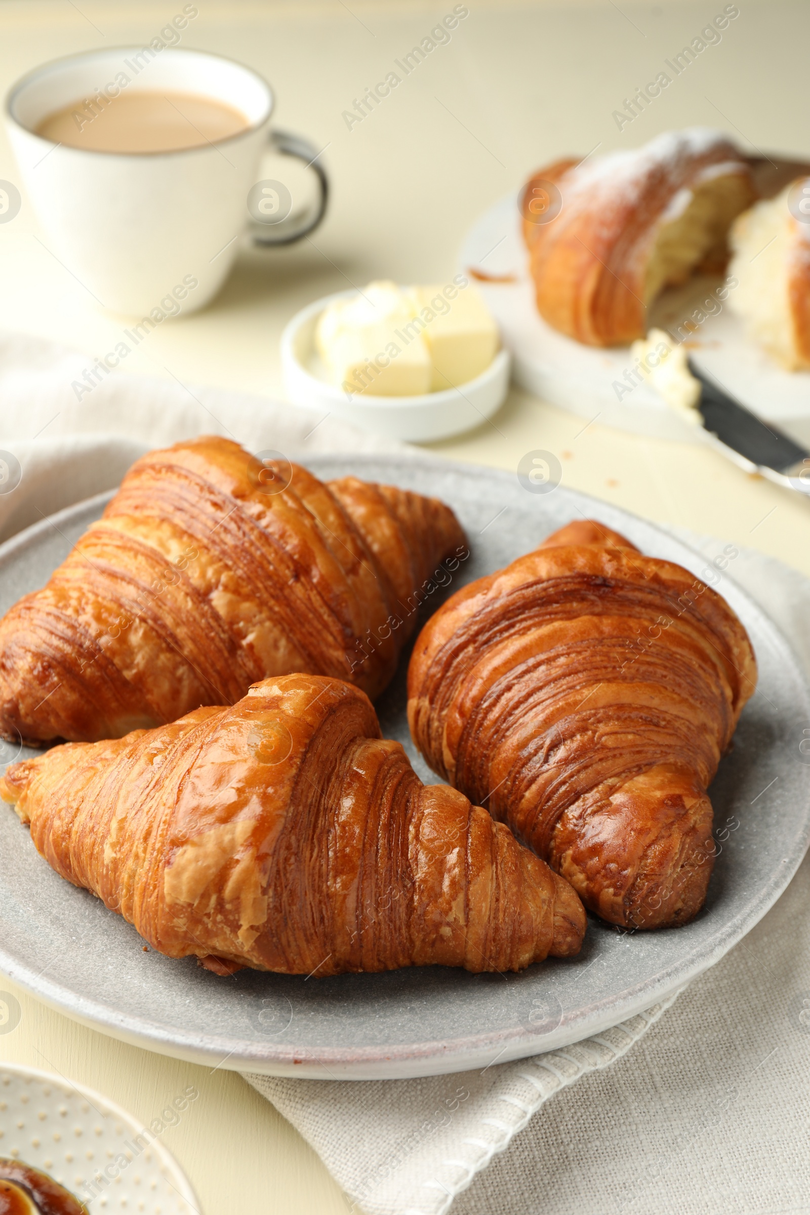 Photo of Plate with tasty croissants on beige table, closeup